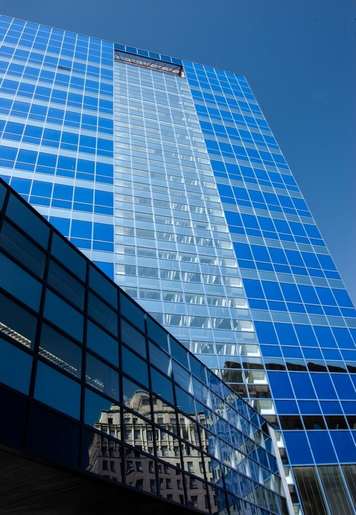 Fachada de edificio corporativo moderno de cristal azul en contrapicado representando la visión de negocio global de MGC Legal.